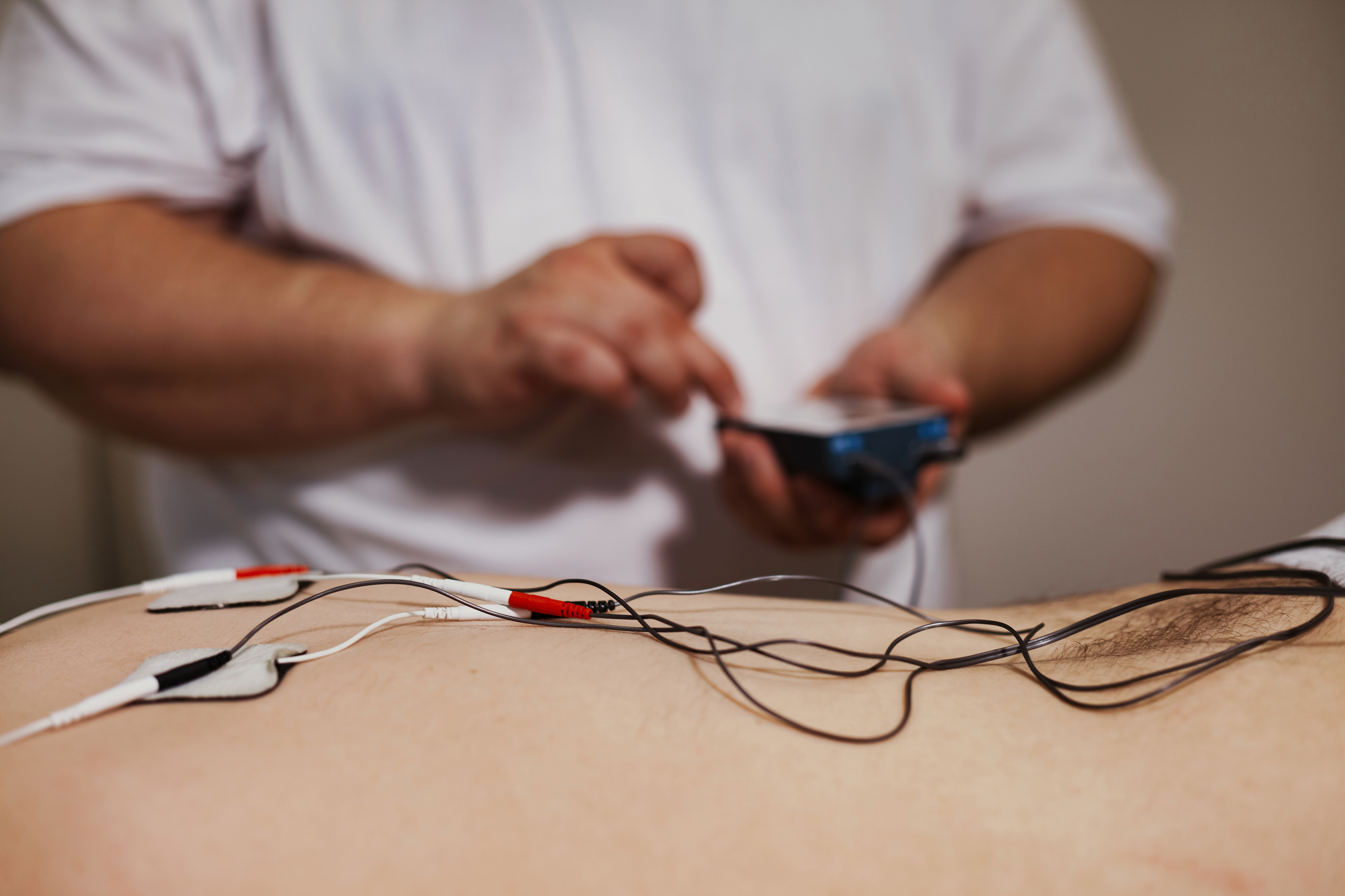 Persona recibiendo tratamiento con microcorrientes para el dolor, electrodos en la espalda y ambiente clínico moderno
